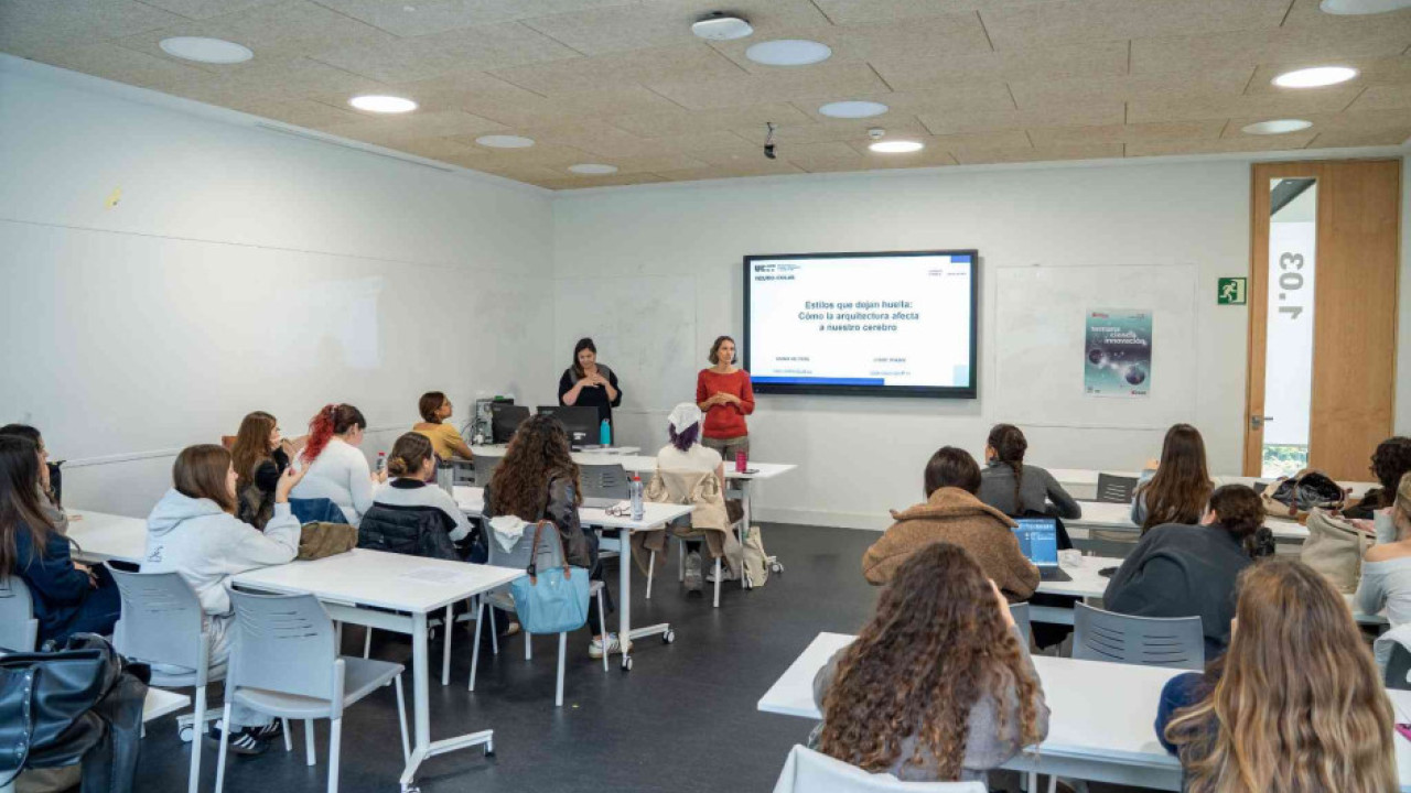 ChatGPT Plus  En un aula luminosa, dos mujeres dan una charla sobre cómo la arquitectura afecta al cerebro ante un grupo de estudiantes que las escuchan atentamente.