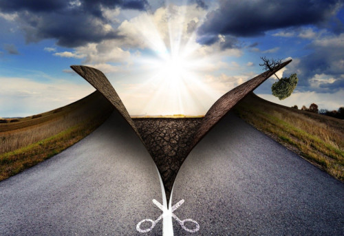 Una tijera corta en dos una carretera de asfalto para mostrar un brillante amanecer. 