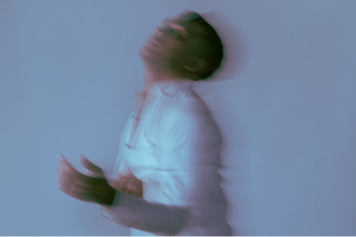 Un hombre con camisa blanca posa en un entorno borroso con los ojos cerrados