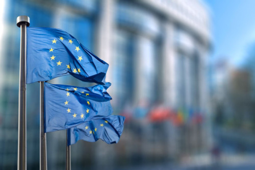Tres banderas de la Unión Europea frente a la difuminada sede de Bruselas