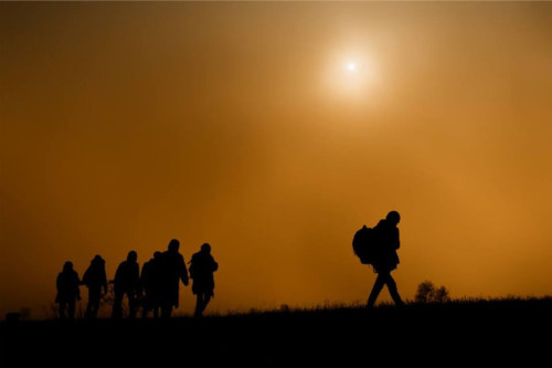 Siete figuras humanas con mochila viajan al atardecer